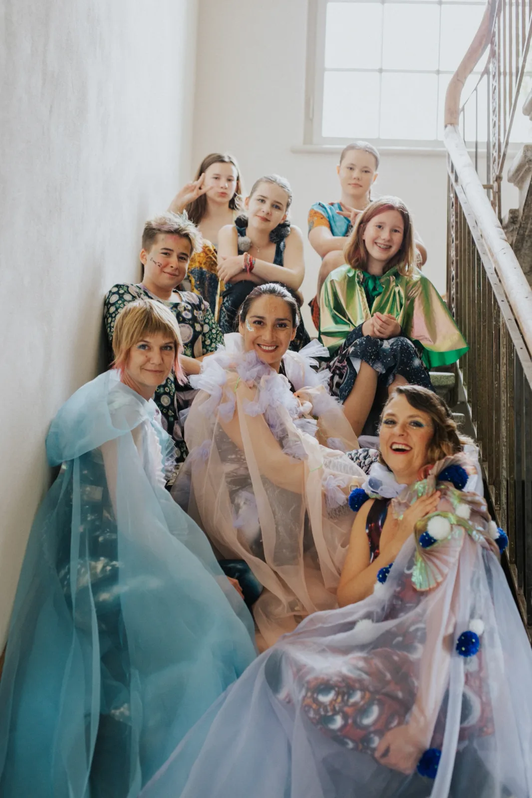 Group portrait of performers in translucent and iridescent costumes on a stairwell.