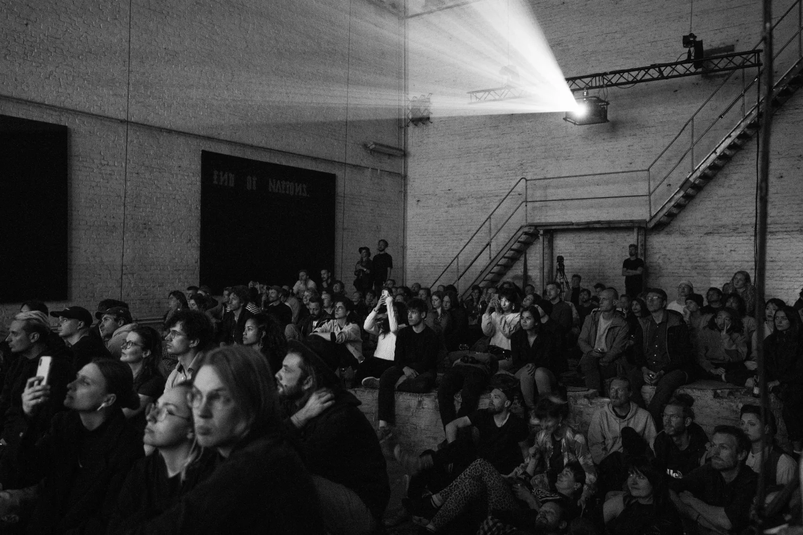 Black-and-white view of a large seated audience watching the performance inside the industrial Monopol hall.