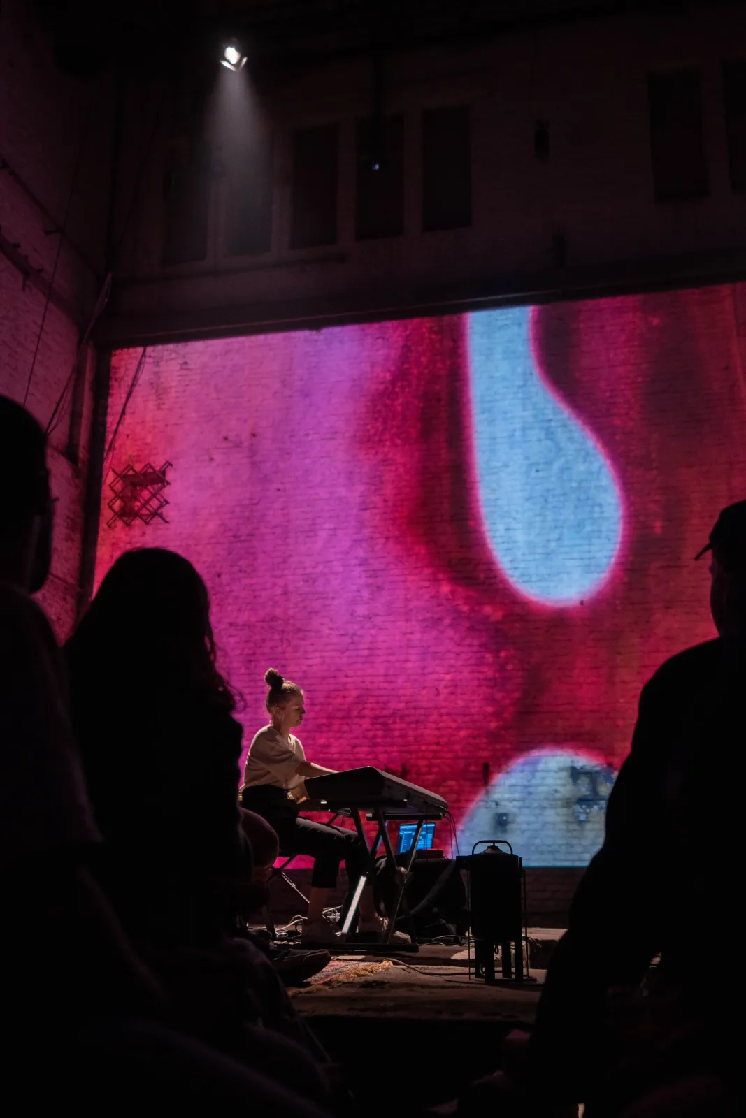 Portrait view of YANA playing a keyboard with a bright magenta and blue microscopic projection behind her.
