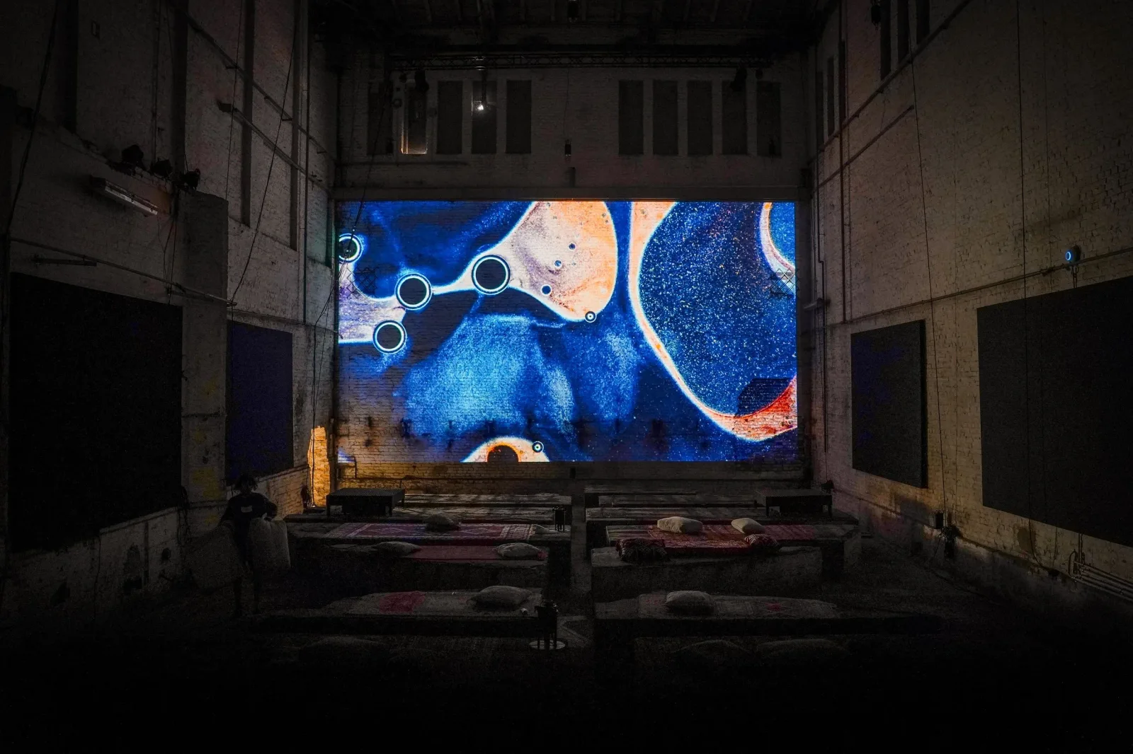 Wide view of the Monopol industrial hall with blue and orange microscopic imagery projected across a brick wall.